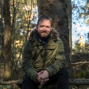 Portrett av Tord Helsingeng sittende under et tre i skogen